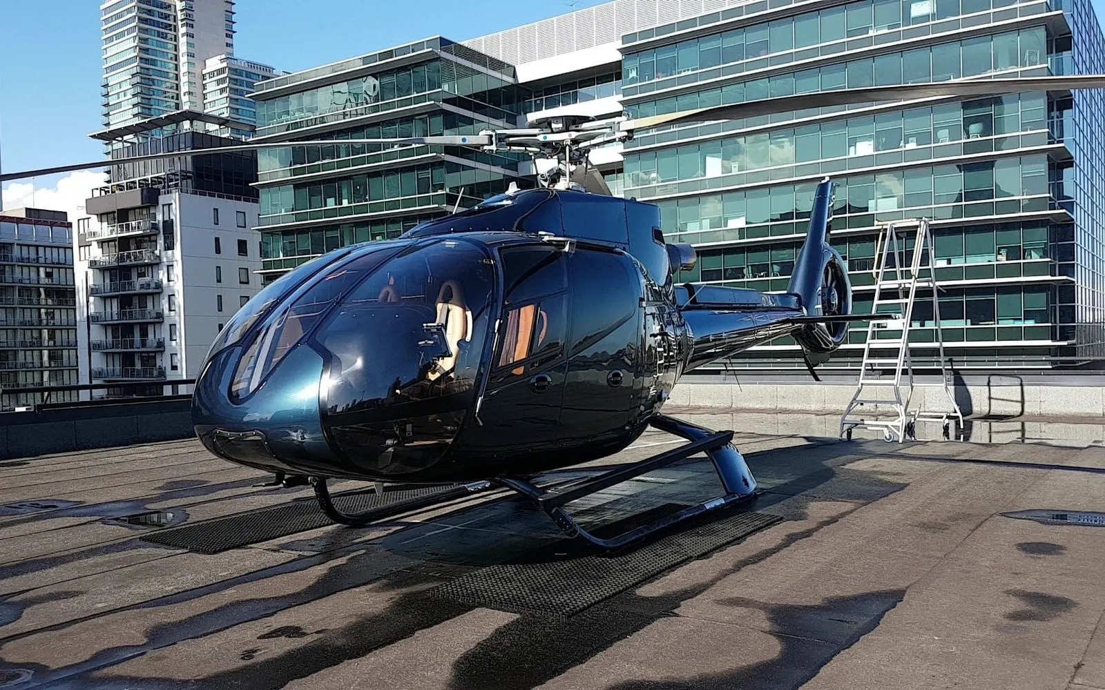 Dark helicopter on an urban rooftop helipad against a city skyline